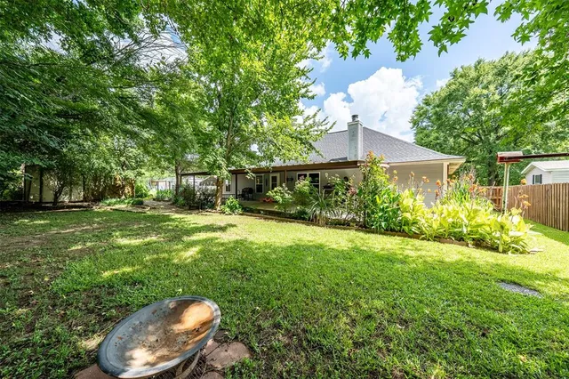 a backyard of a house with table and chairs plants and large tree