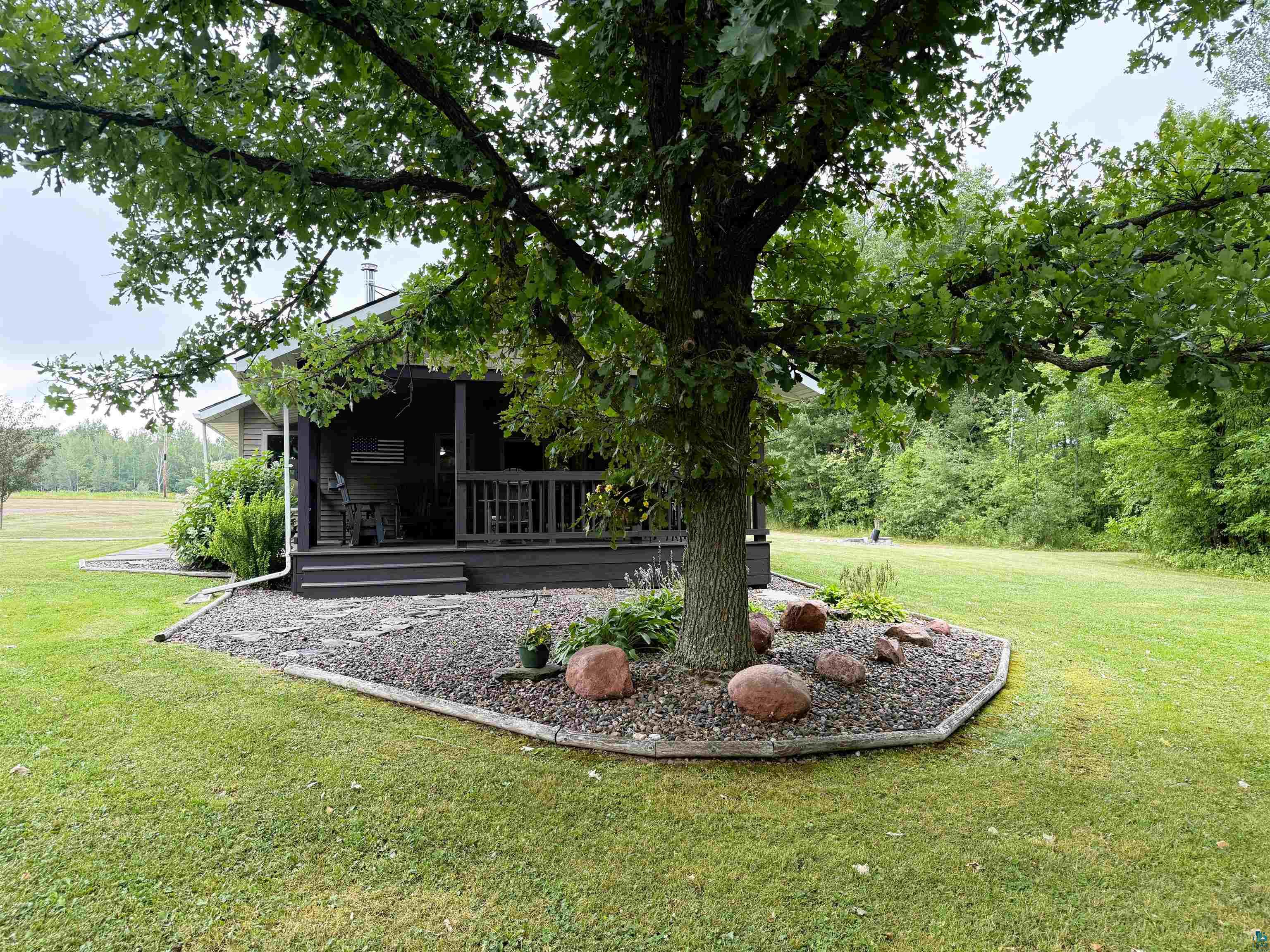 5080 Tower Road Moose Lake, MN 55767 - Photo 33 of 49 Expansive lawn with mature trees, a gravel landscaping bed, and a covered porch