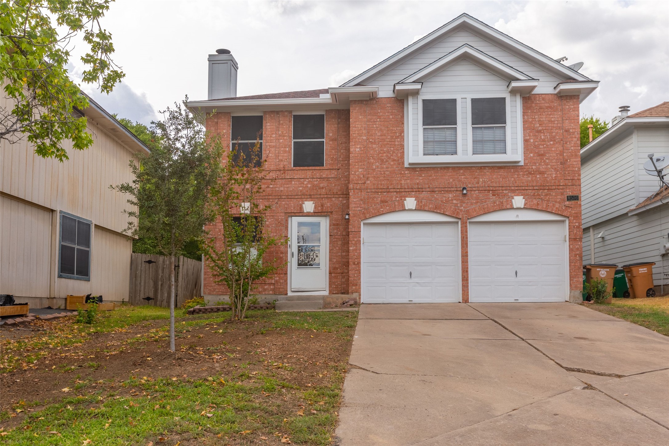 Brick-clad two-story residence featuring a front entry door with a storm door, an attached two-car garage with arched accents, and a prominent gable dormer with horizontal siding