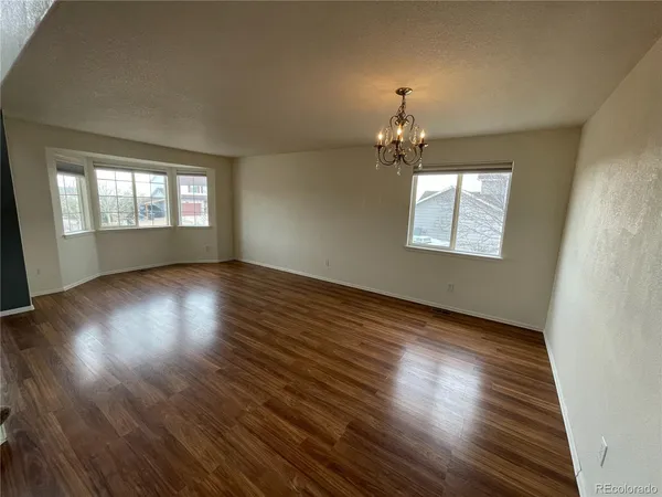 an empty room with wooden floor chandelier and windows