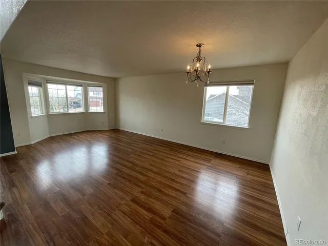 an empty room with wooden floor chandelier and windows