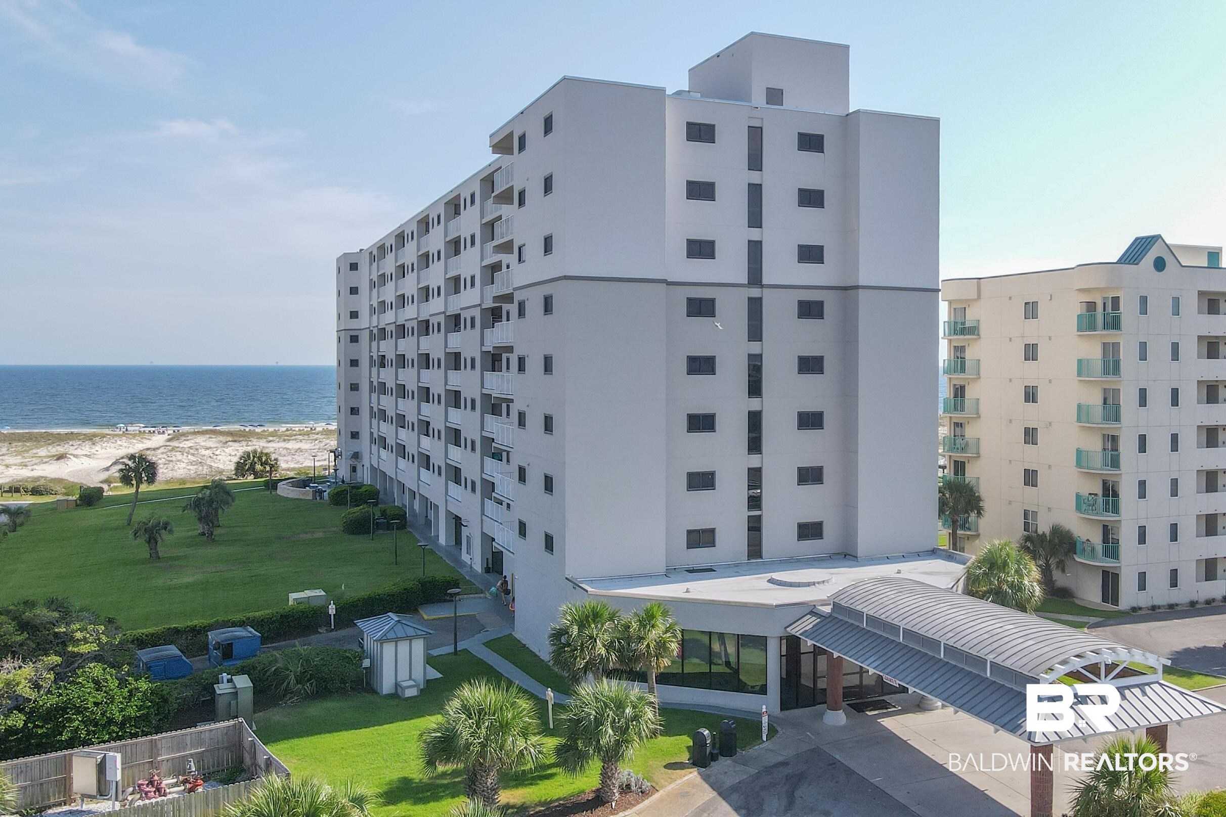 375 Plantation Road, Unit 5105 Gulf Shores, AL 36542 - Photo 1 of 9 Multi-story building with a covered entry, featuring balconies on multiple levels, a green lawn, and direct beach access