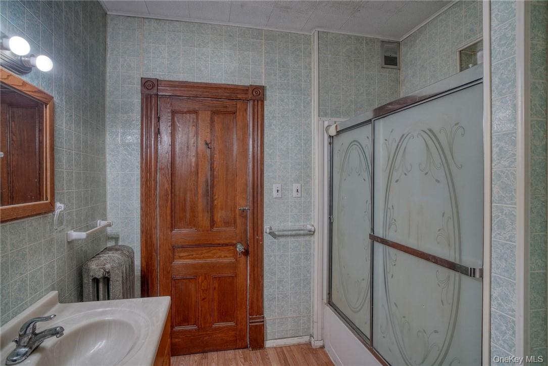 32 Balding Avenue Poughkeepsie, NY 12601 - Photo 18 of 39 Bathroom featuring radiator heating unit, tile walls, bath / shower combo with glass door, vanity, and hardwood / wood-style flooring