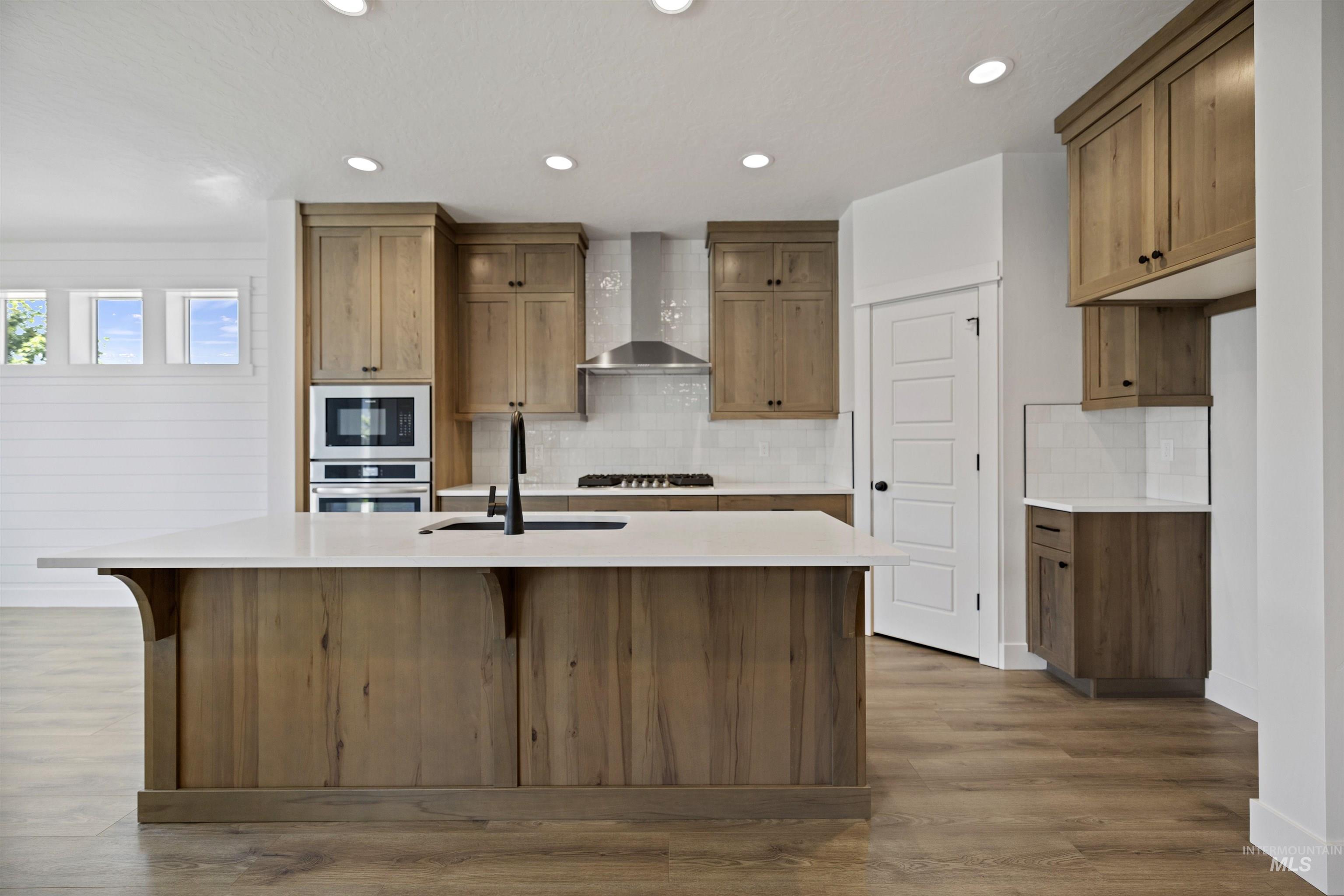 3515 South El Rio Avenue Boise, ID 83709 - Photo 15 of 47 Kitchen with wall chimney range hood, an island with sink, decorative backsplash, light countertops, and stainless steel oven