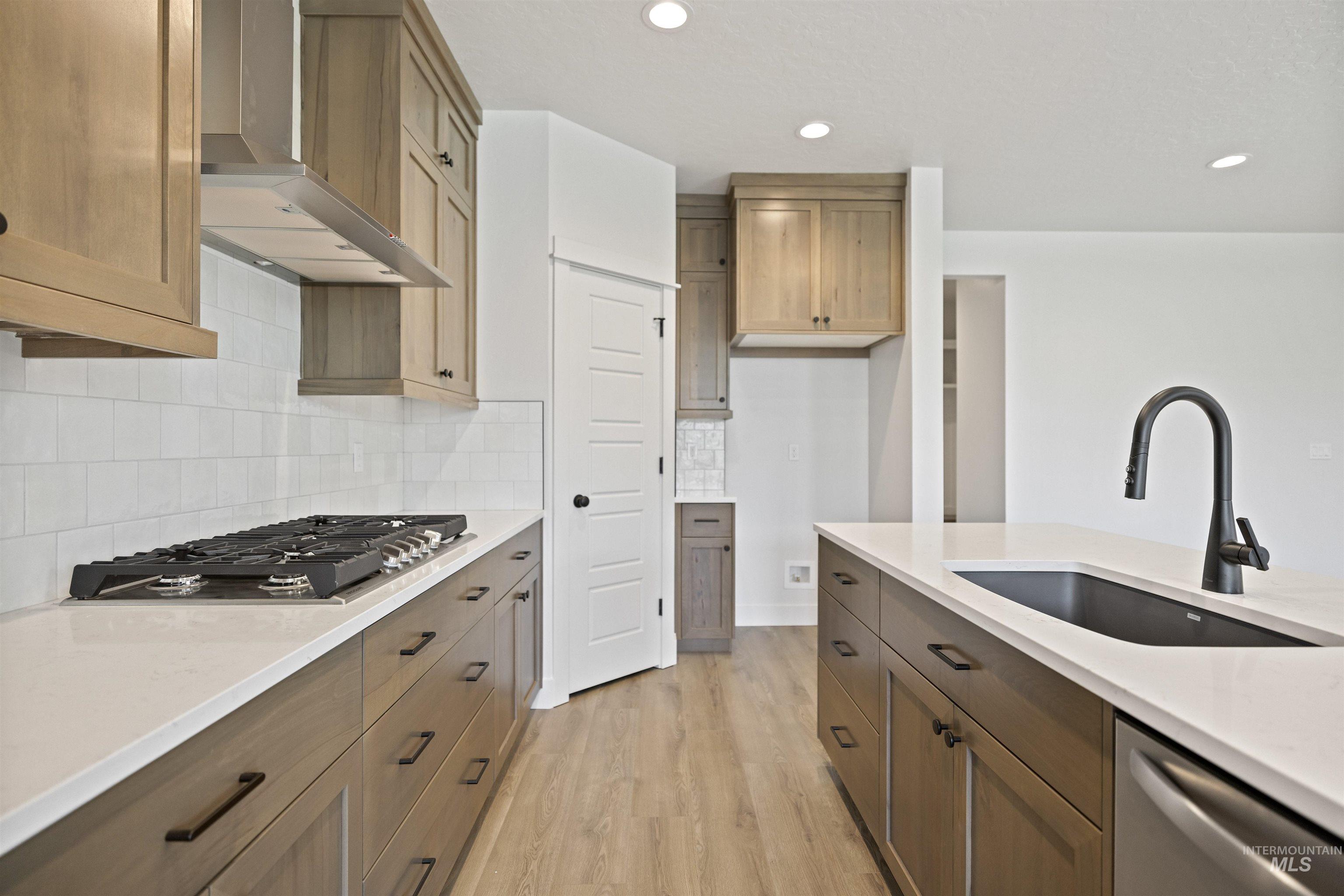 3515 South El Rio Avenue Boise, ID 83709 - Photo 16 of 47 Kitchen featuring wall chimney range hood, appliances with stainless steel finishes, light wood finished floors, light countertops, and decorative backsplash