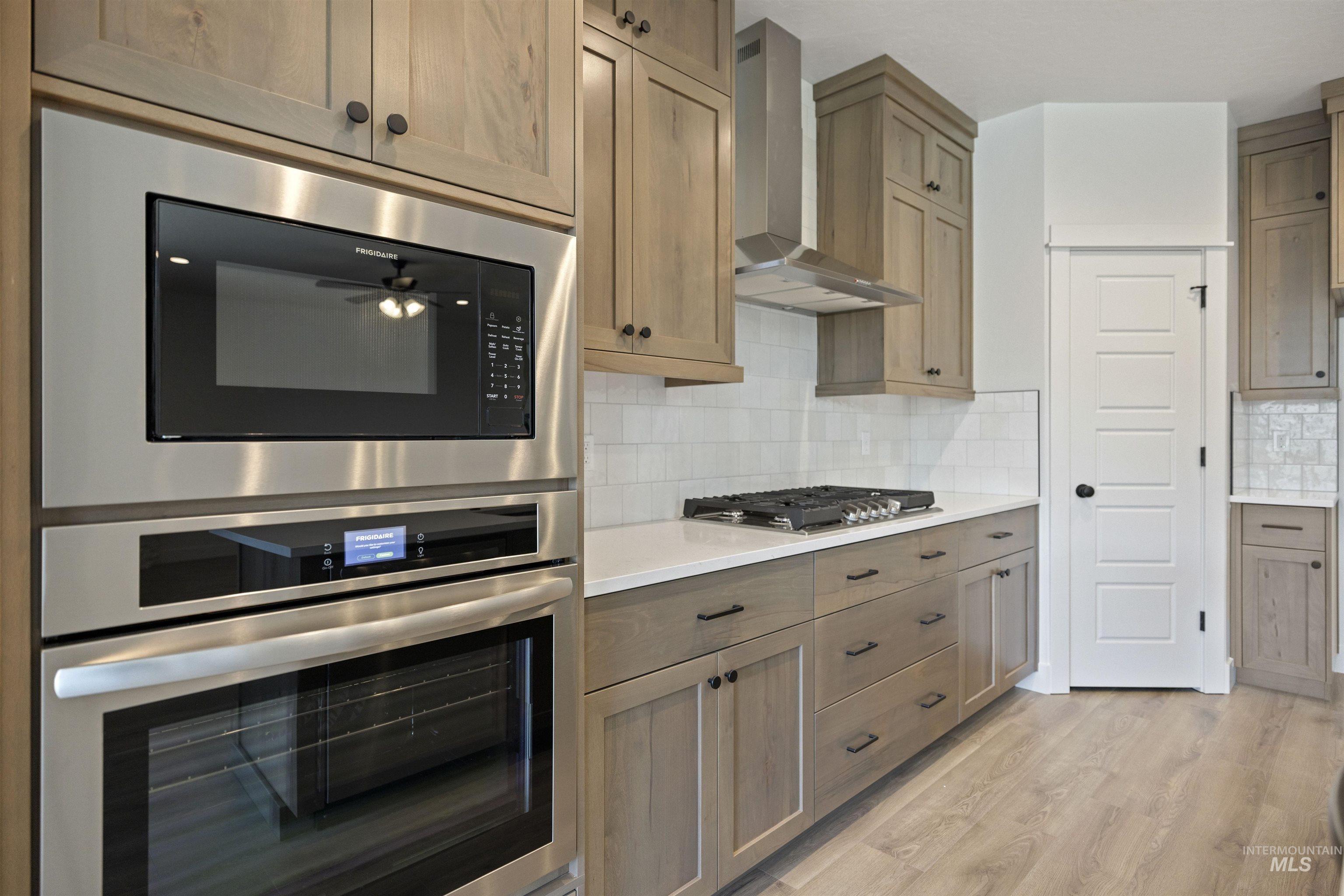 3515 South El Rio Avenue Boise, ID 83709 - Photo 17 of 47 Kitchen featuring stainless steel appliances, wall chimney range hood, light wood-style flooring, light countertops, and decorative backsplash