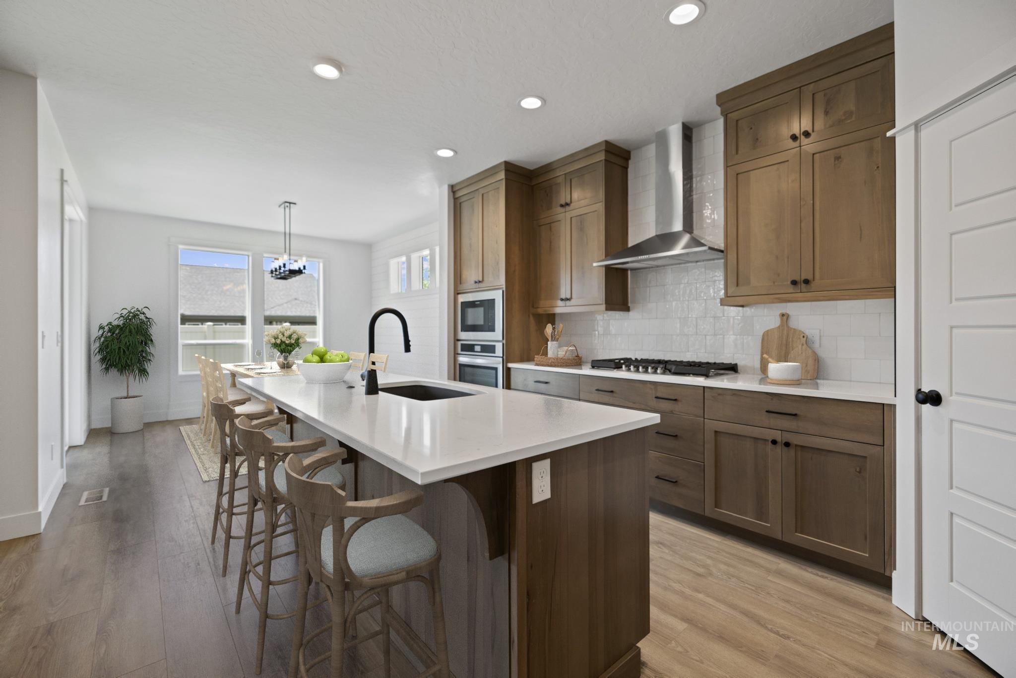 3515 South El Rio Avenue Boise, ID 83709 - Photo 18 of 47 Kitchen with wall chimney exhaust hood, a kitchen island with sink, backsplash, a kitchen breakfast bar, and light countertops