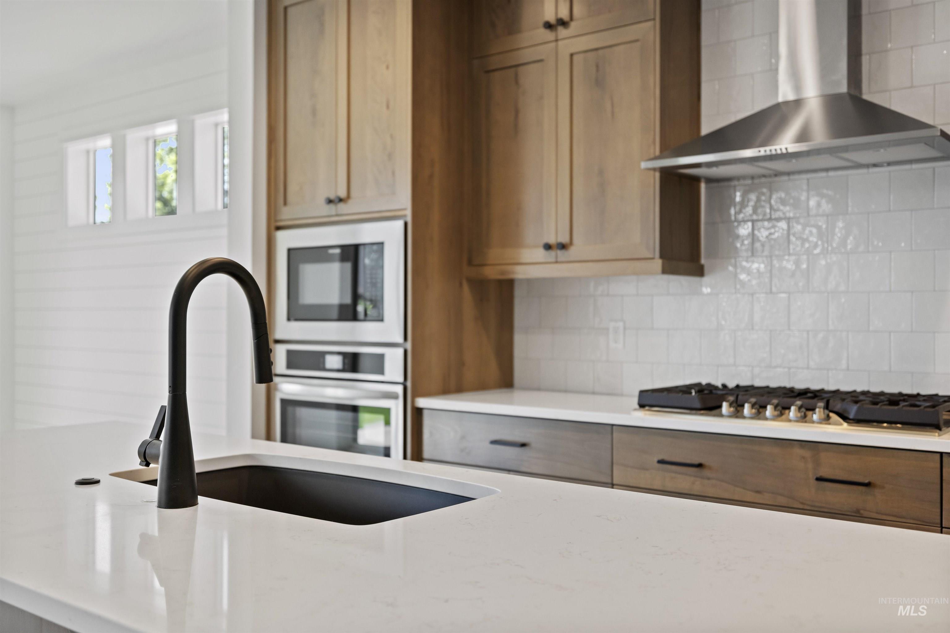 3515 South El Rio Avenue Boise, ID 83709 - Photo 19 of 47 Kitchen featuring wall chimney range hood, stainless steel appliances, backsplash, and light stone countertops