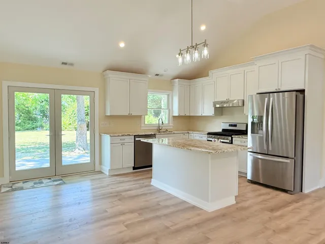 a kitchen with stainless steel appliances granite countertop a refrigerator a sink dishwasher a stove and white countertops with wooden floor