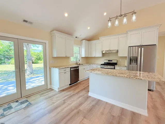 a kitchen with stainless steel appliances granite countertop a refrigerator a sink dishwasher a stove and white countertops with wooden floor