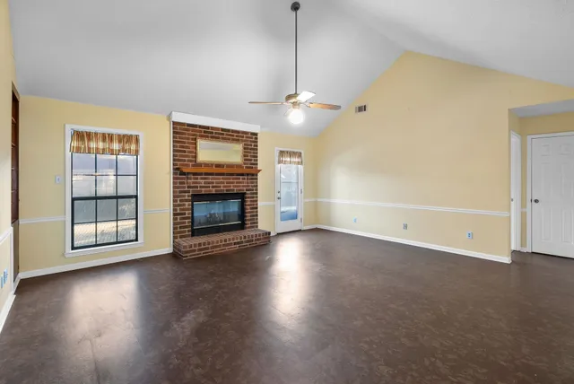 an empty room with wooden floor fireplace and windows
