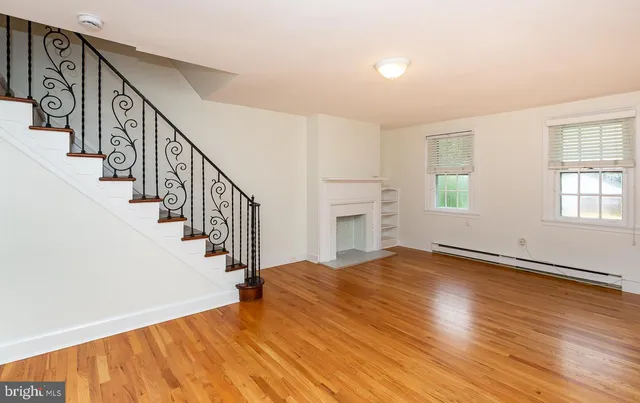 a view of an empty room with wooden floor and fan