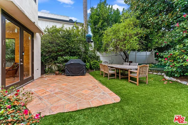 a view of a backyard with table and chairs potted plants and large tree