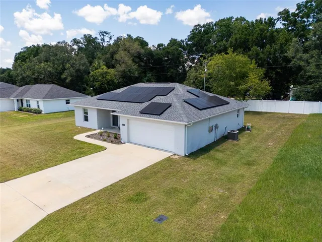 a view of a white house next to a yard with plants and large trees