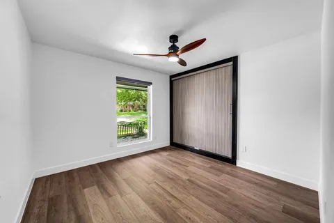an empty room with wooden floor chandelier fan and windows