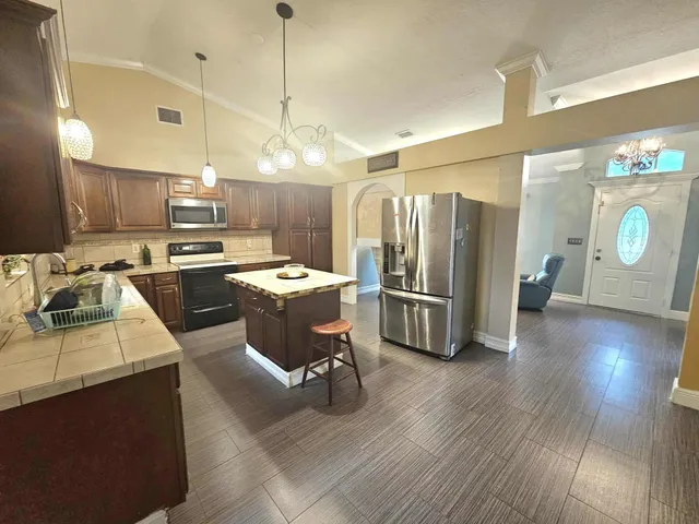 a kitchen with stainless steel appliances granite countertop a refrigerator a sink dishwasher a stove and a dining table with wooden floor