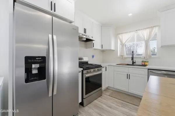 a kitchen with stainless steel appliances granite countertop a refrigerator a sink a stove and white cabinets with wooden floor