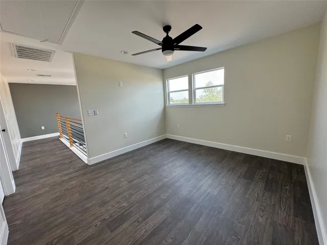 an empty room with wooden floor a ceiling fan and windows