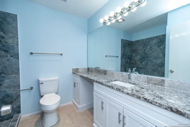 a bathroom with a granite countertop toilet a sink and a mirror