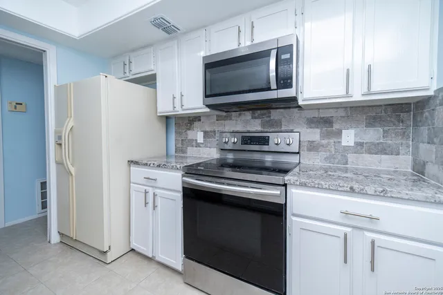a kitchen with stainless steel appliances granite countertop white cabinets a refrigerator and a stove top oven