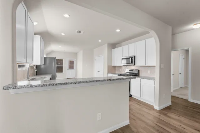 a large kitchen with granite countertop a sink and white cabinets