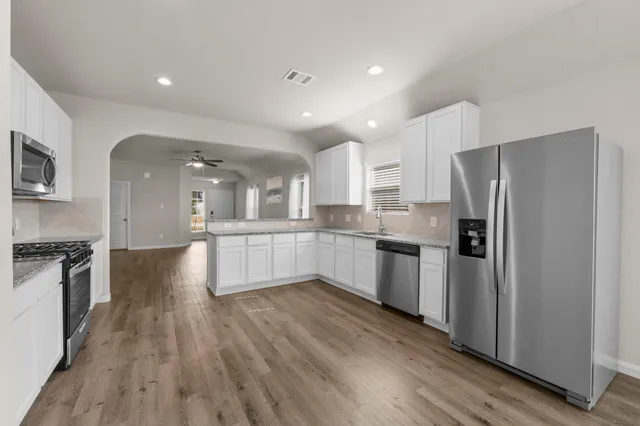 a large kitchen with a center island wooden floor stainless steel appliances and cabinets