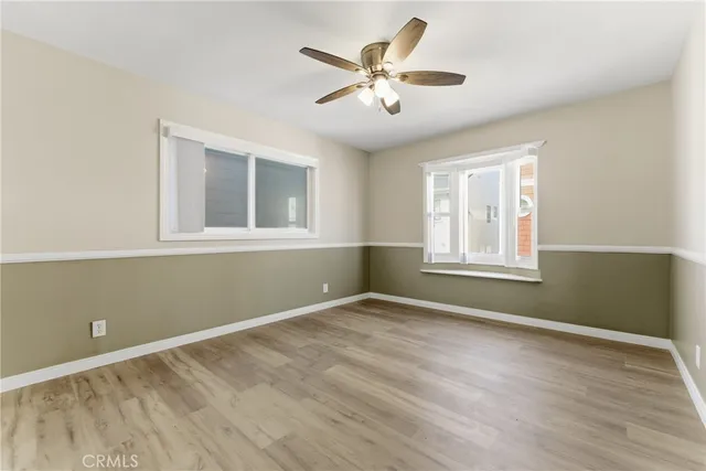 an empty room with wooden floor fan and windows