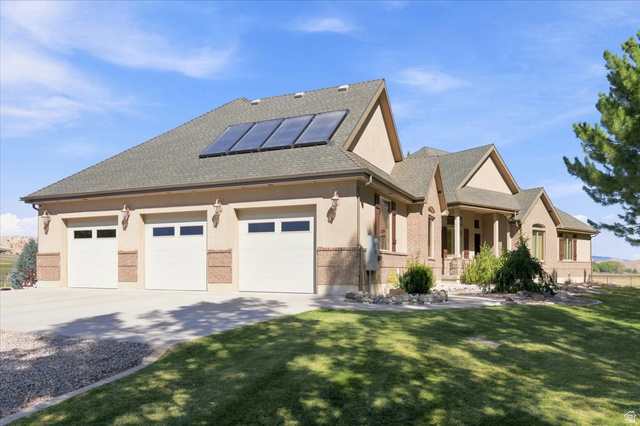 11290 South Southfield Road Mayfield, UT 84643 - Photo 18 of 103 Stucco and brick exterior with a three-car garage, solar panels, a covered entry, and a manicured lawn