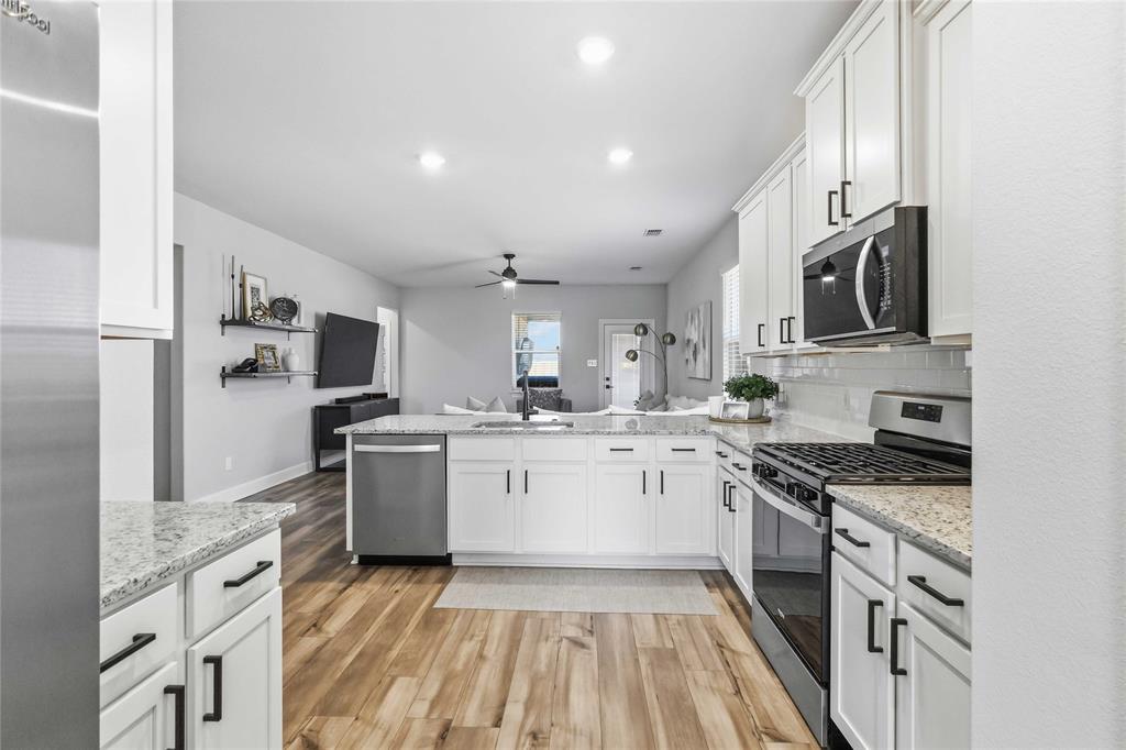 1012 Calhoun Drive Anna, TX 75409 - Photo 13 of 39 Modern kitchen featuring white cabinetry with black hardware, stainless steel appliances, granite-look countertops, and wood-finish flooring