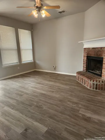 a view of an empty room with wooden floor fireplace and a window