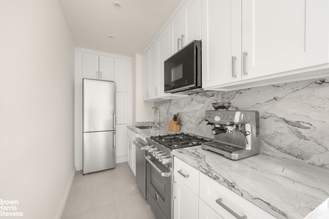 211 East 18th Street, Unit 3R Manhattan, NY 10003 - Photo 5 of 10 a kitchen with stainless steel appliances granite countertop white cabinets stove a microwave and a refrigerator