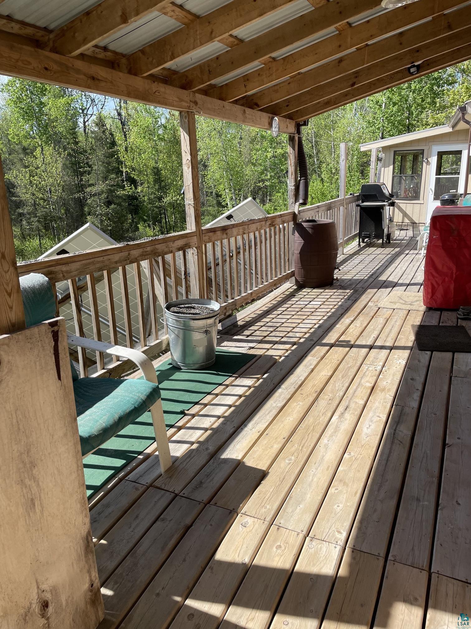 1152 Fernberg Road Ely, MN 55731 - Photo 4 of 24 Expansive wood deck with a partial overhead covering, featuring a wood railing and a natural treed backdrop