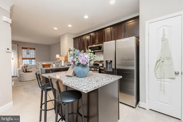 a kitchen with stainless steel appliances granite countertop a dining table chairs and refrigerator