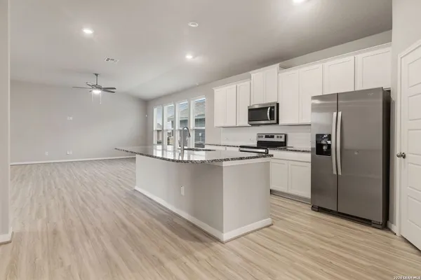 a kitchen with stainless steel appliances a refrigerator stove a sink and white cabinets with wooden floor