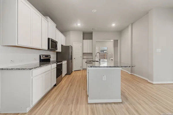 a kitchen with stainless steel appliances granite countertop a refrigerator a sink dishwasher a stove and white cabinets with wooden floor