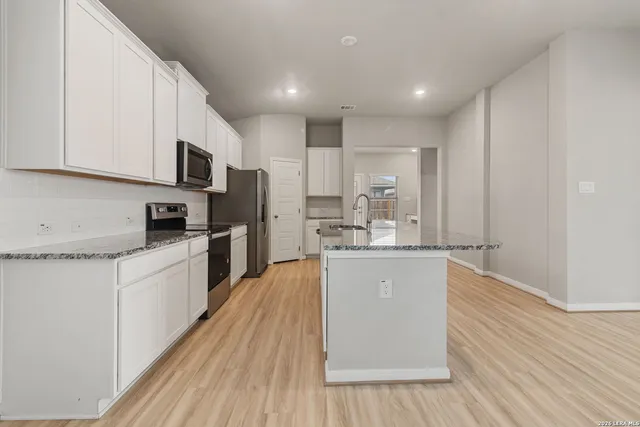 a kitchen with stainless steel appliances granite countertop a refrigerator a sink dishwasher a stove and white cabinets with wooden floor