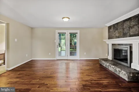 a view of an empty room with wooden floor fireplace and a window