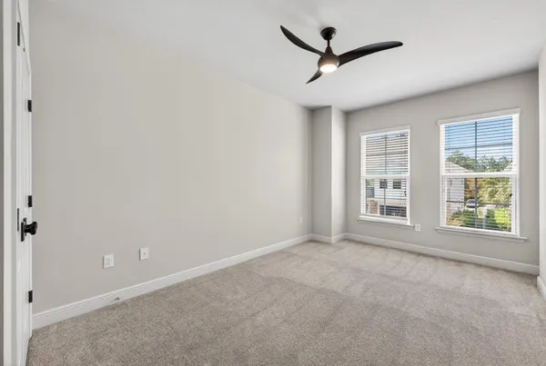 an empty room with a ceiling fan & windows