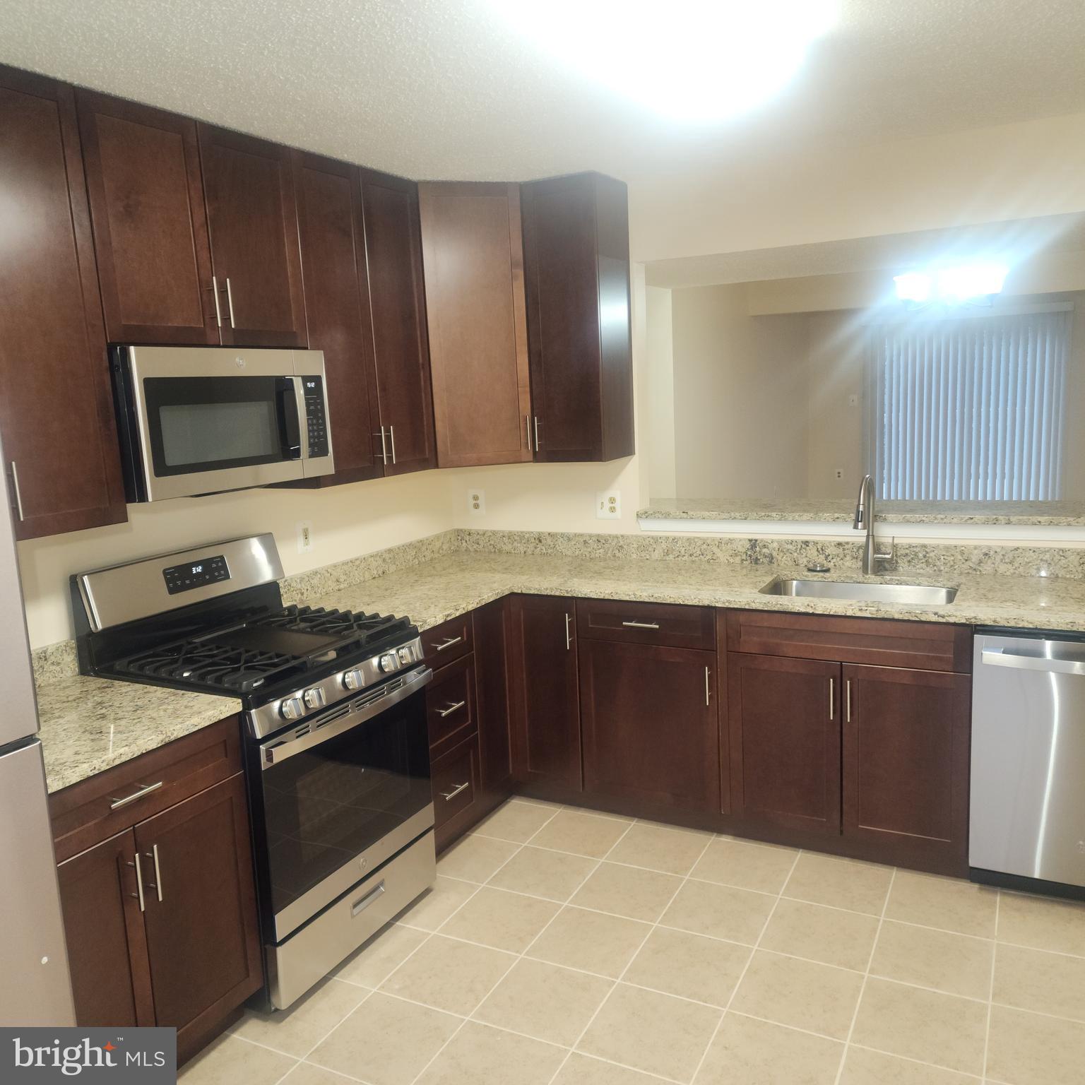 7438 Catterick Court Baltimore, MD 21244 - Photo 11 of 27 a kitchen with granite countertop a stove a microwave and wooden cabinets