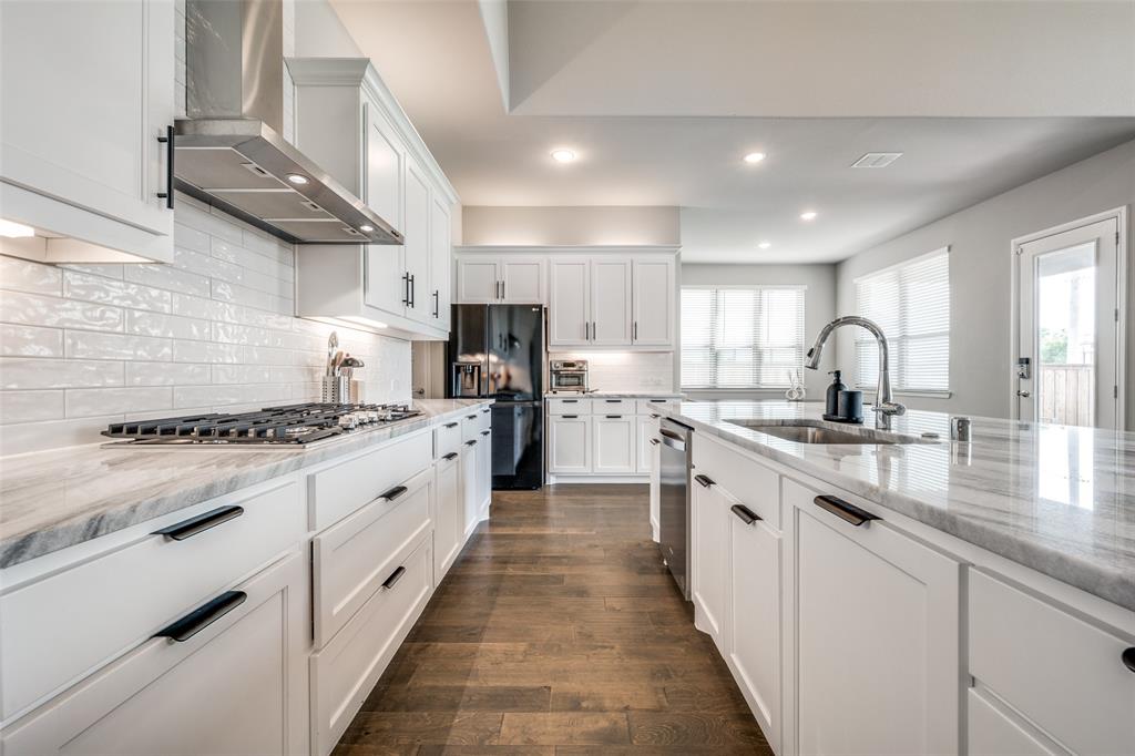 16564 Creek Plum Road Frisco, TX 75033 - Photo 9 of 30 Kitchen with light stone countertops, white cabinets, dark wood-type flooring, recessed lighting, and black fridge