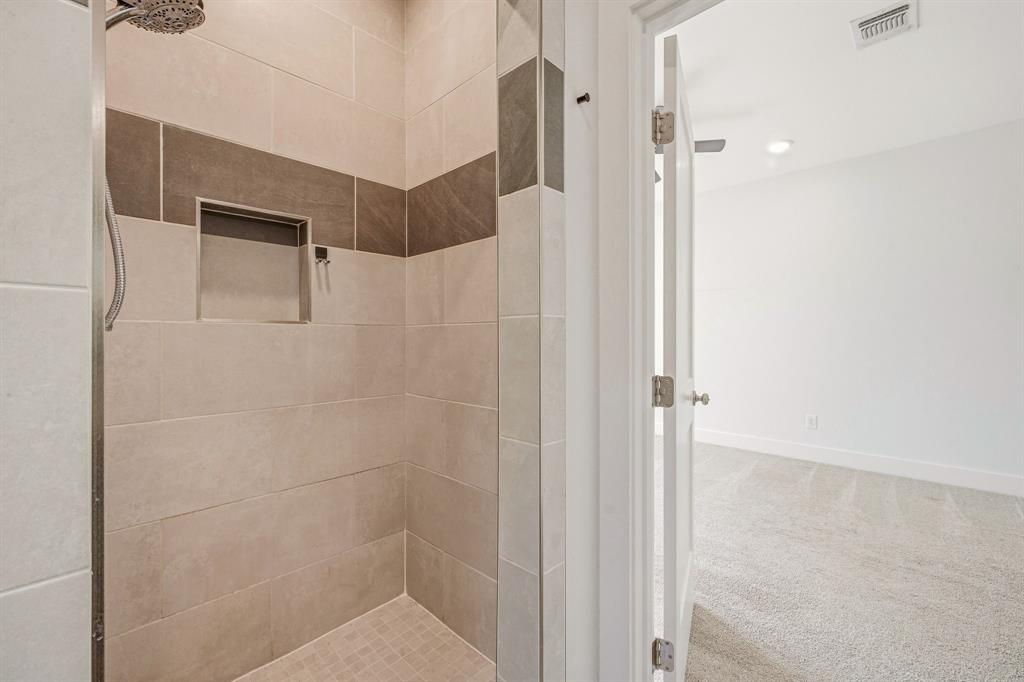 745 North Miller Avenue Stephenville, TX 76401 - Photo 18 of 31 Shower enclosure with light-toned rectangular wall tiles, a contrasting dark horizontal accent band, and a built-in shower niche