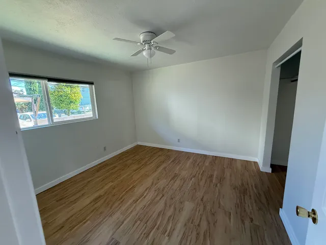 an empty room with wooden floor fan and windows