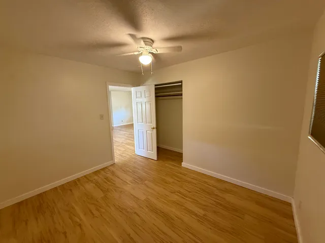 a view of an empty room with wooden floor and a ceiling fan