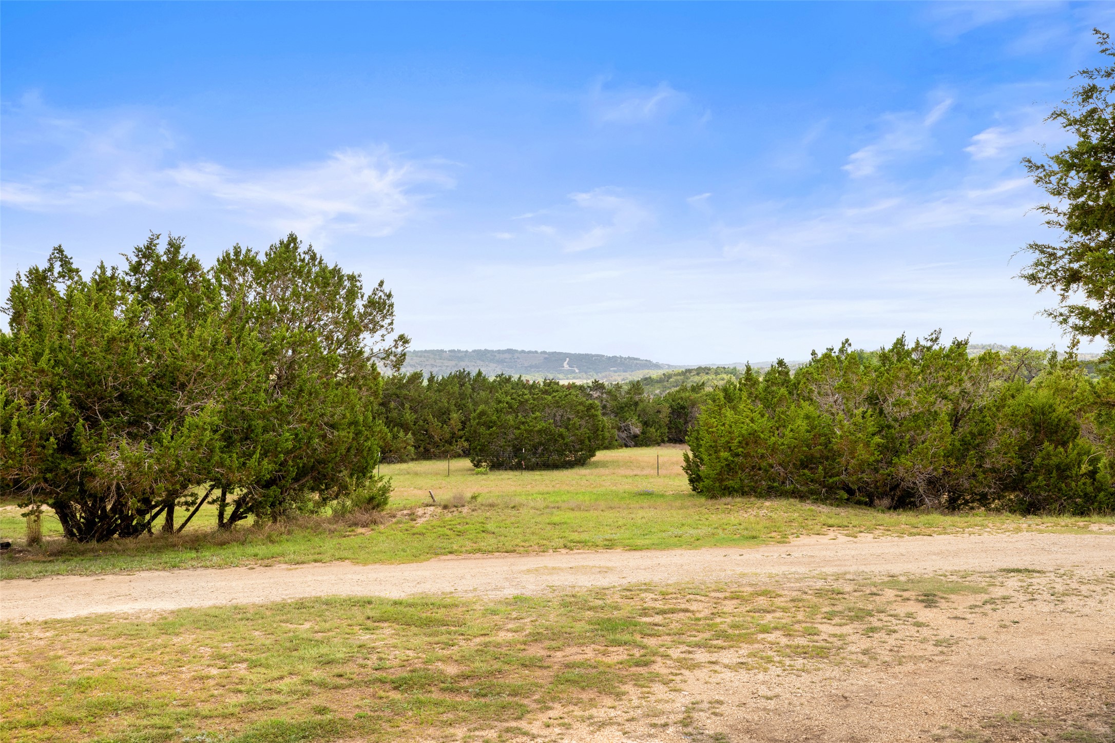 2966 Rm 165 Dripping Springs Dripping Springs, TX 78620 - Photo 8 of 23 Expansive open land with a dirt path, mature green shrubbery, and distant rolling hills