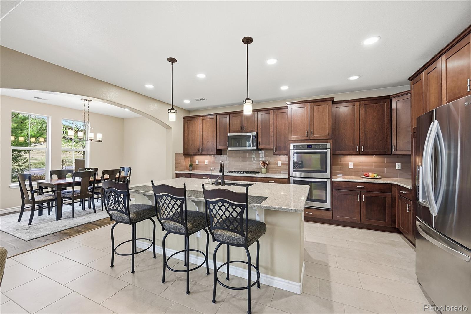 9500 Pendio Court Highlands Ranch, CO 80126 - Photo 4 of 15 a kitchen with stainless steel appliances kitchen island granite countertop a refrigerator a stove a sink a dining table and chairs with wooden floor
