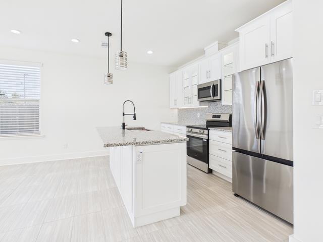 511 Richardson Street Athens, TX 75751 - Photo 10 of 40 Kitchen with appliances with stainless steel finishes, hanging light fixtures, an island with sink, light stone counters, and white cabinets