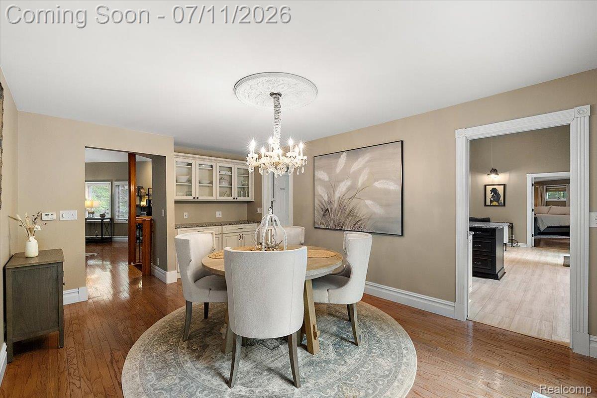 4219 Gardner Road Metamora, MI 48455 - Photo 12 of 87 Dining area featuring hardwood flooring, a crystal chandelier with a decorative ceiling medallion, and a built-in buffet with glass-front cabinetry and a stone countertop