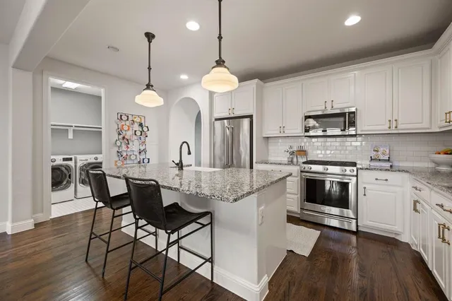 a kitchen with granite countertop a stove a sink island a dining table and chairs with wooden floor