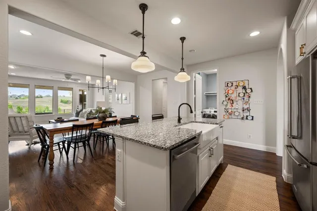 a kitchen with stainless steel appliances granite countertop a stove a refrigerator a kitchen island a dining table and chairs with wooden floor