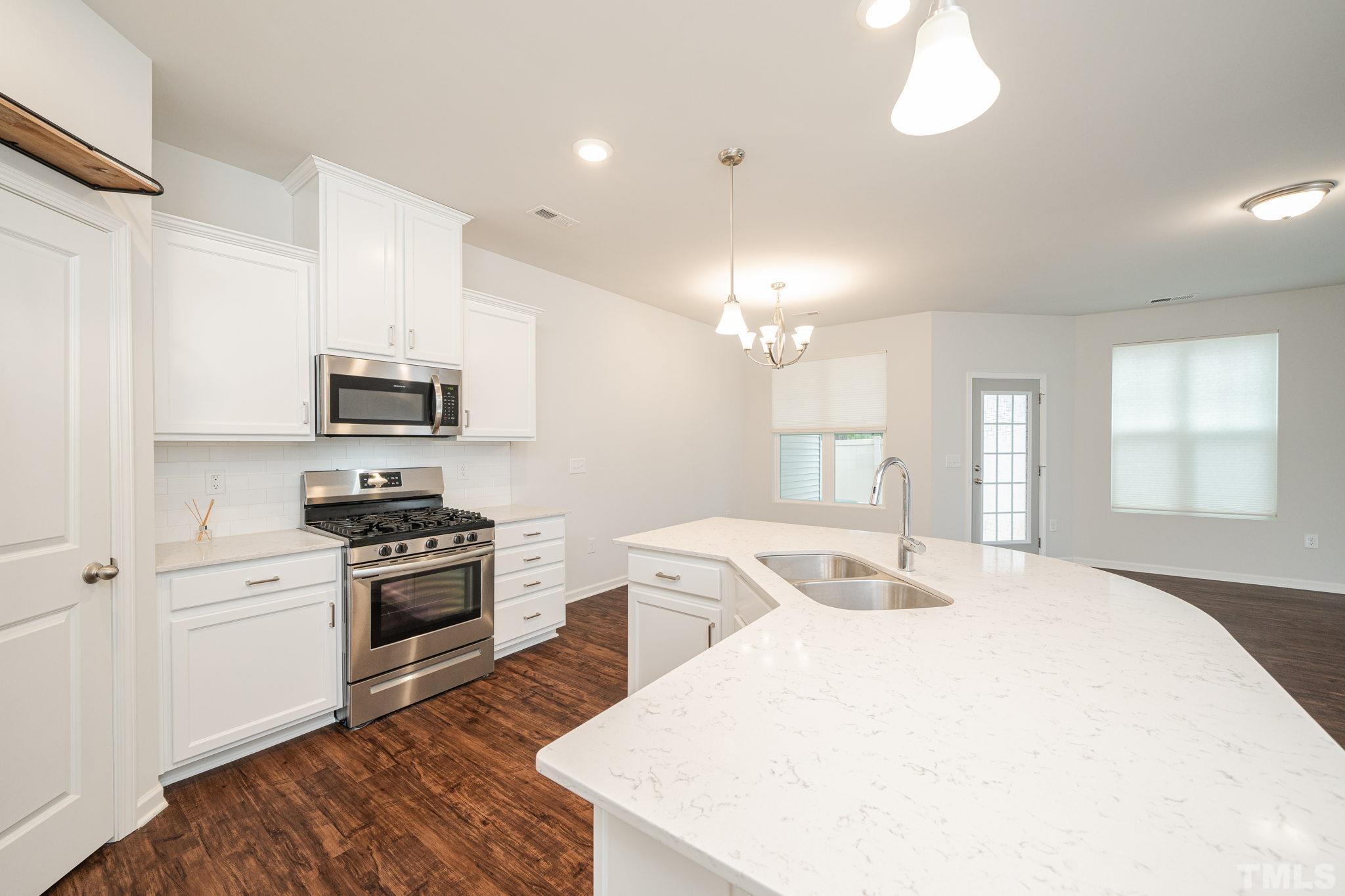 a large white kitchen with stainless steel appliances granite countertop a stove a sink dishwasher and a refrigerator with wooden floor